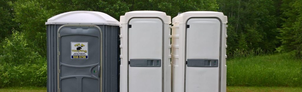 Three portable toilets in a grassy outdoor setting