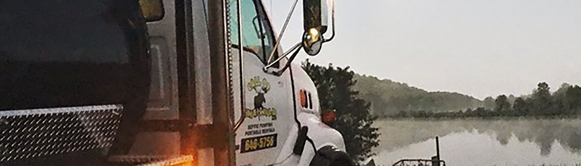 Septic services truck by a foggy lake during sunrise