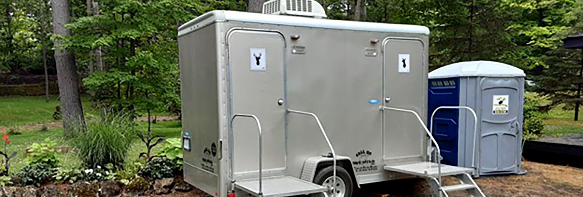 Portable stainless steel restroom trailer in a wooded outdoor setting