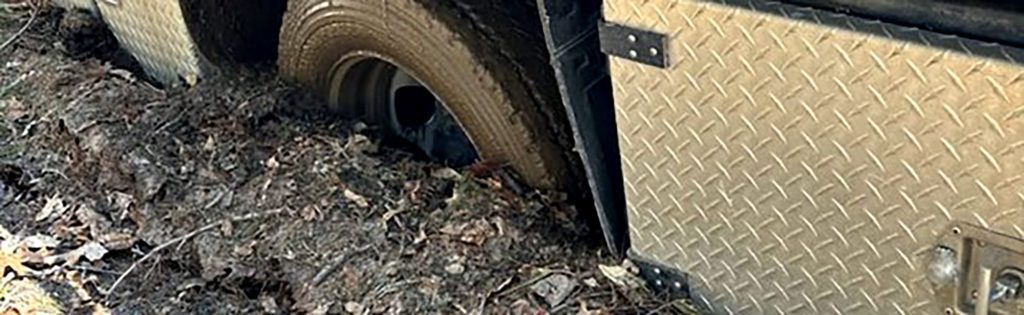Utility vehicle tire stuck in muddy terrain while travelling through rough ground