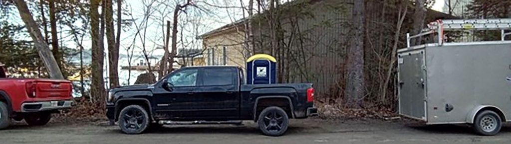Black pickup truck carrying portable toilet in rural area