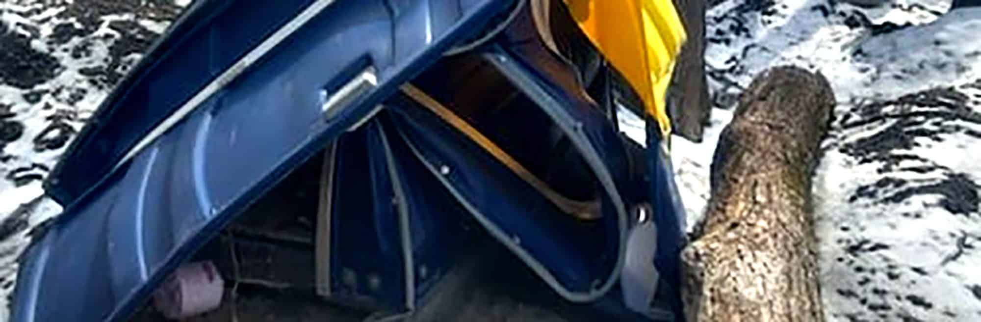 Blue portable toilet wrecked in snowy forest after tree collision