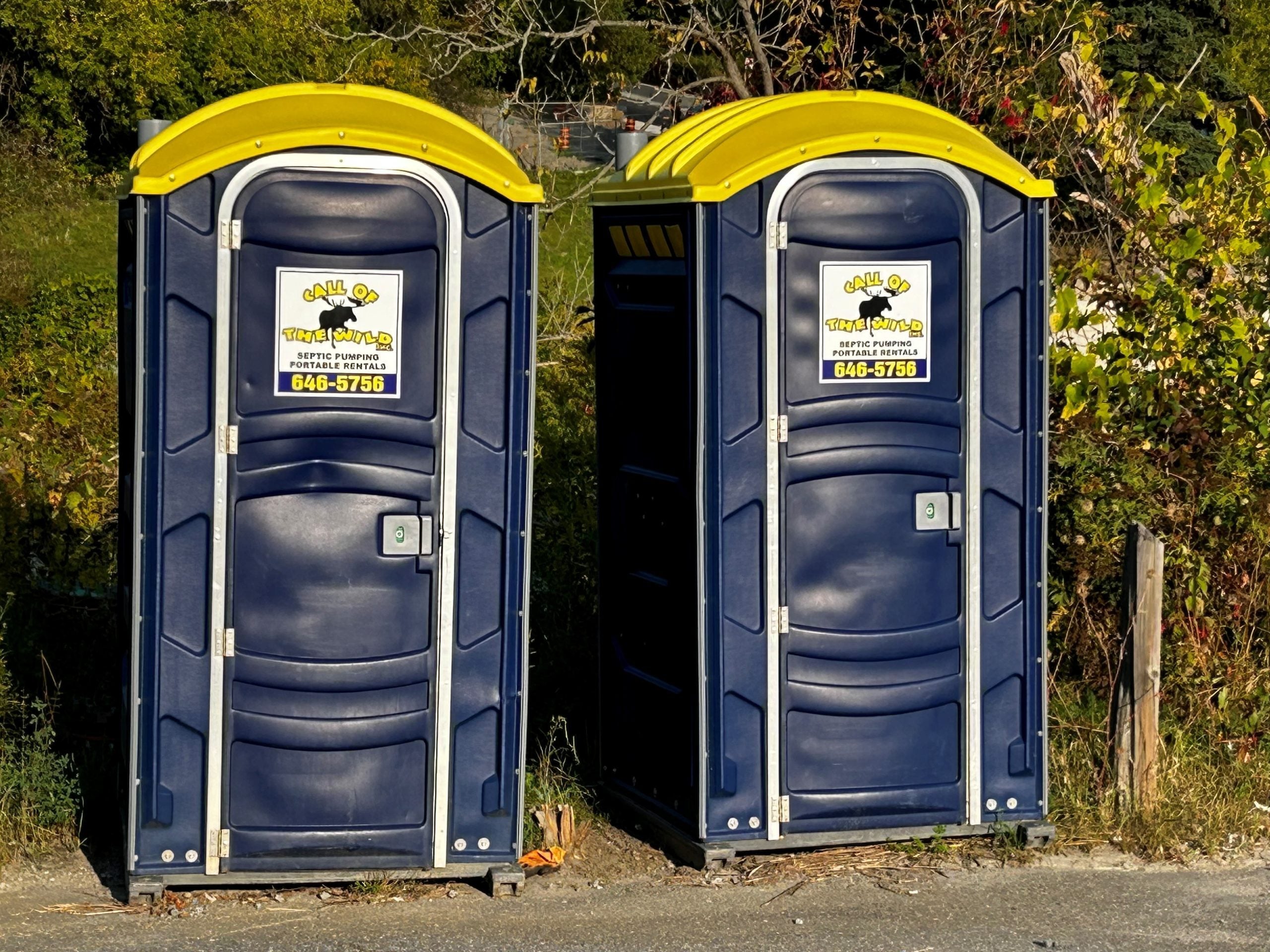 Two blue portable toilets with yellow roofs in outdoor setting