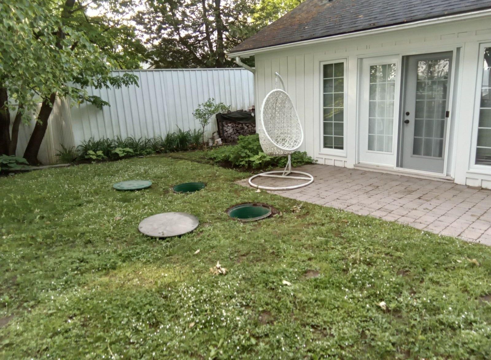 Backyard with septic tank covers and a hanging chair by a white house