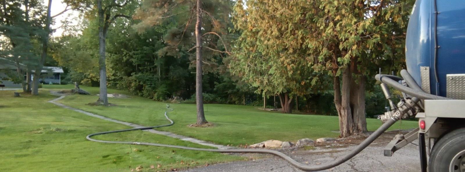 Septic service truck with hose in a lush yard during autumn