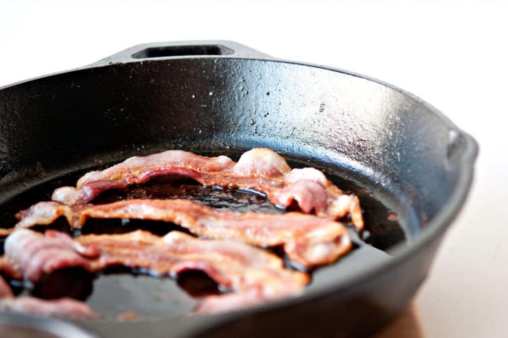Crispy bacon cooking in a cast iron skillet