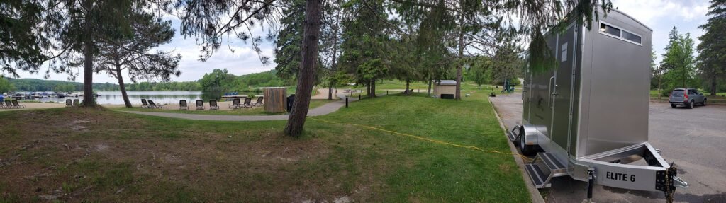 Luxury portable restroom trailer by forested lakeside park with picnic area