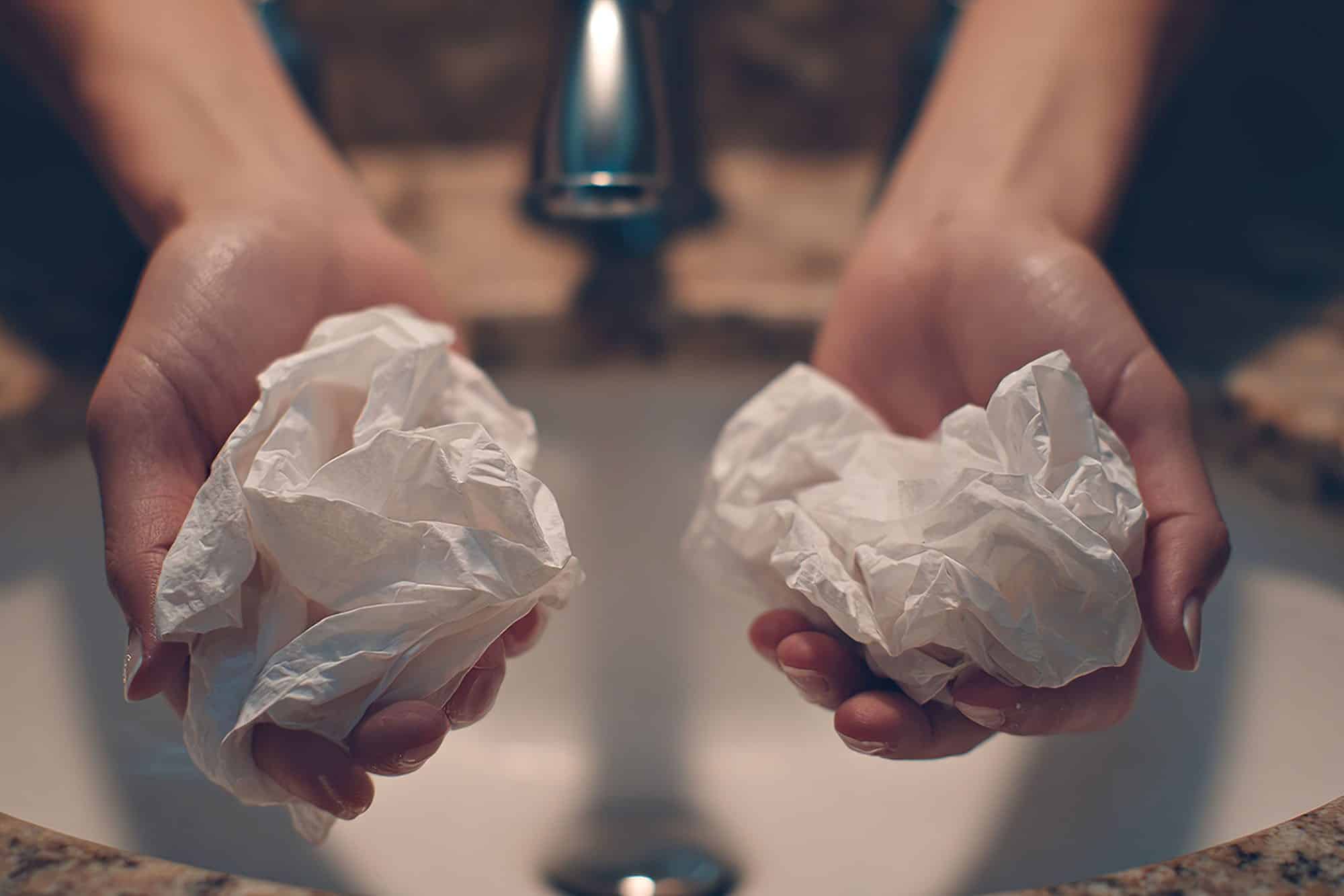 Hands over sink holding crumpled tissues