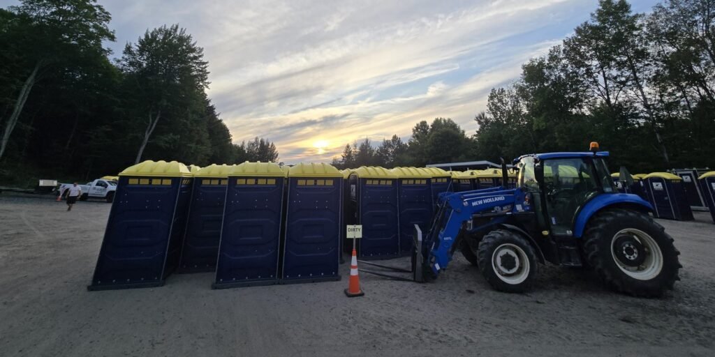 Tractor placing portable toilets at outdoor event site with sunset