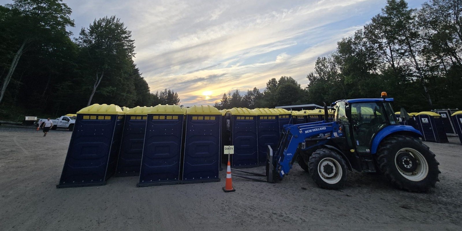 Tractor placing portable toilets at outdoor event site with sunset
