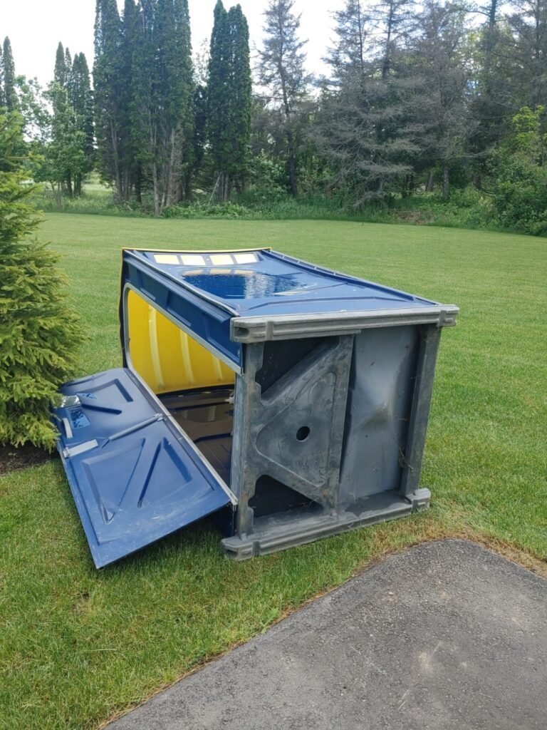 Overturned portable toilet on grassy lawn near trees